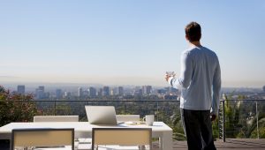 wealth-man-using-laptop-on-balcony-overlooking-city